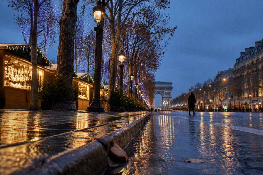 An empty Paris avenue in early winter dusk with street lamps glowing and wet reflective pavement