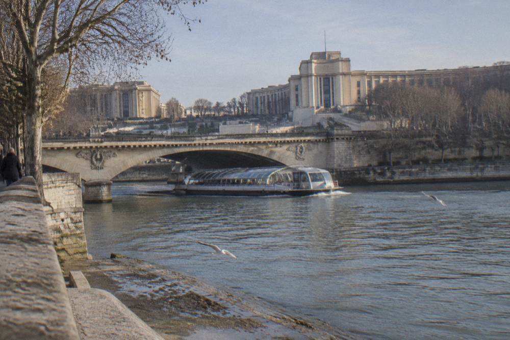 A lunch cruise boat passing a stone bridge on the Seine with the riverbanks in winter light