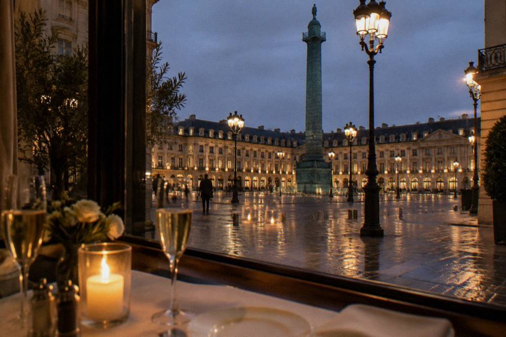 Set dinner table with glassware and candles beside a window with city lights at night