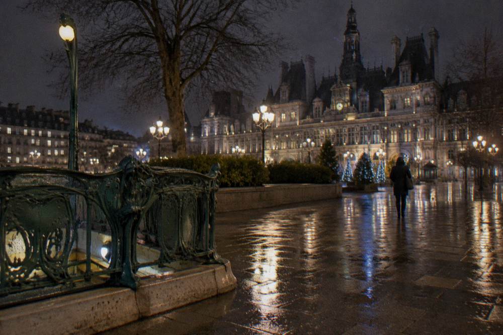 Night city street with wet pavement reflecting festive lights and a metro entrance sign