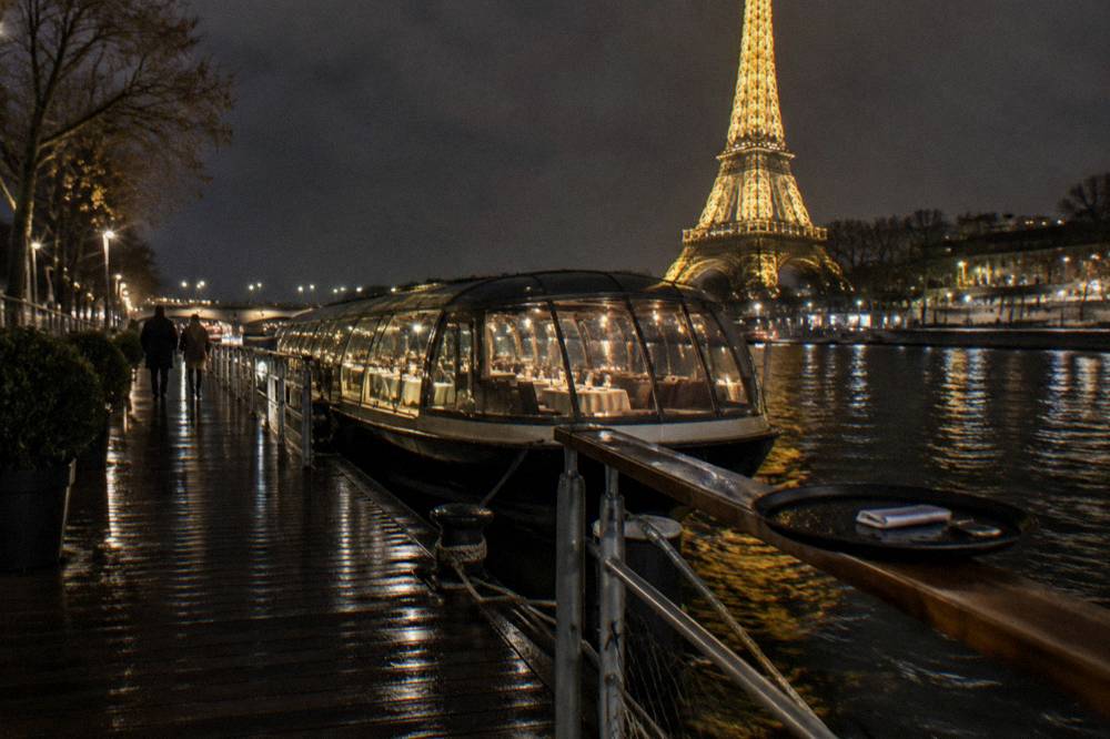 Glass-covered pleasure boat on the Seine at night with city lights reflecting on the water