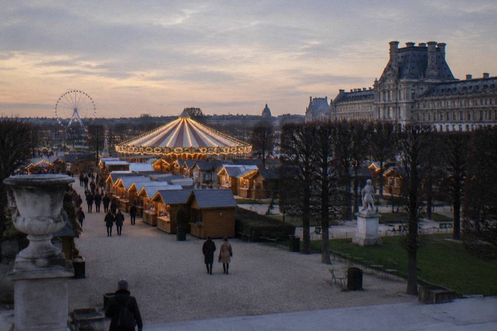 A Christmas market chalet row with garlands and a lit tree above a city plaza
