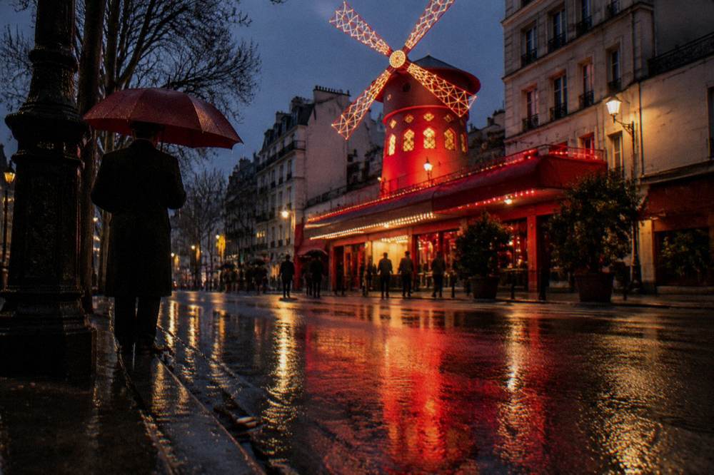 A lit cabaret facade and glowing street lamps on a Paris boulevard at night
