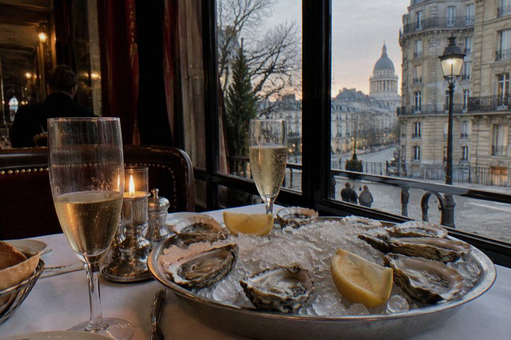 A platter of fresh oysters on ice with lemon wedges beside champagne glasses on a restaurant table