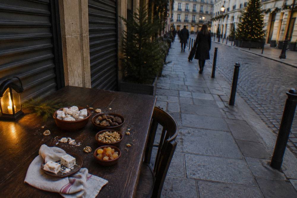 A wooden table laid with small dishes of nougat, dried figs, nuts and candied fruit for a dessert spread
