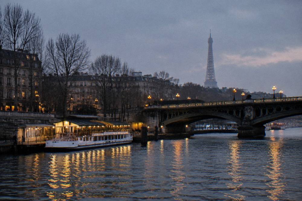 Illuminated bridge over the Seine at dusk with city lights reflecting on the water