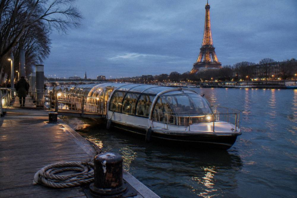 A departure pier along the Seine with a covered passenger boat moored beside it in evening light