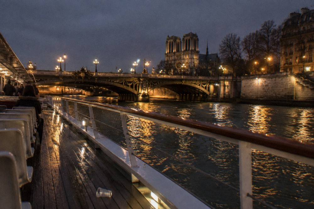 A open-deck passenger boat gliding past illuminated bridges on the Seine after dark