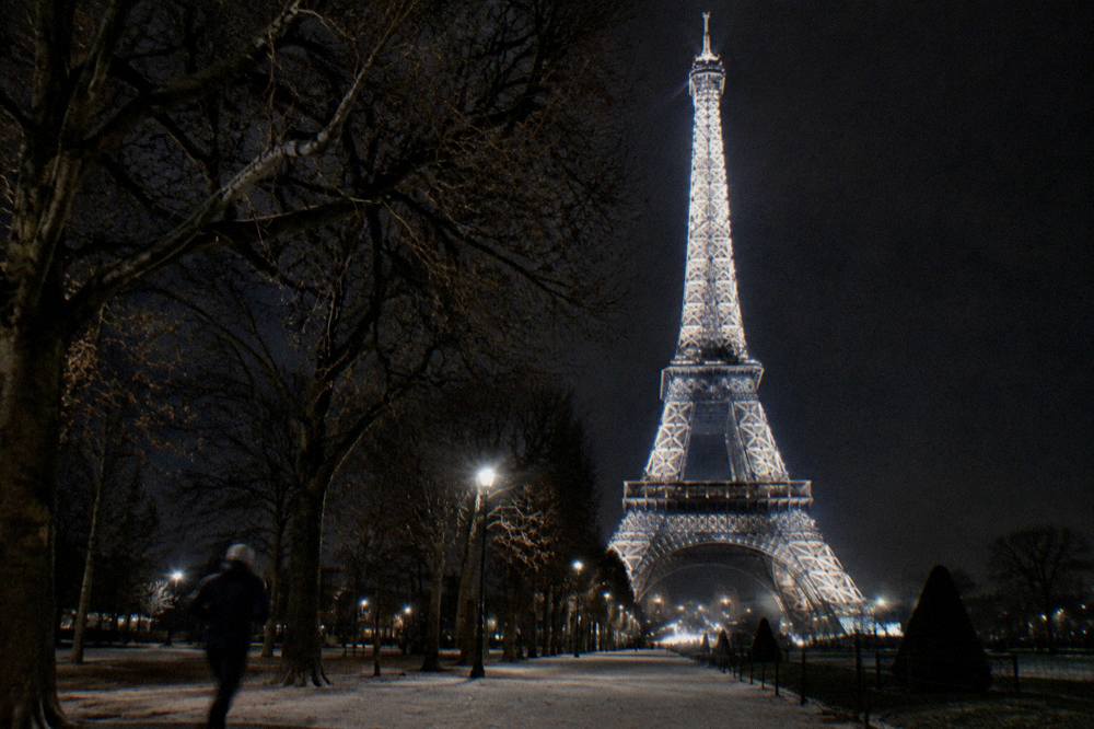 The Eiffel Tower sparkling with white lights against a dark sky above the Seine
