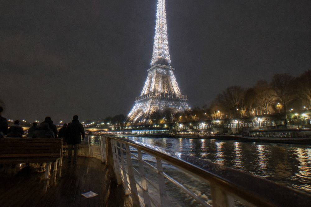 A illuminated Eiffel Tower seen from a riverboat on the dark Seine at night