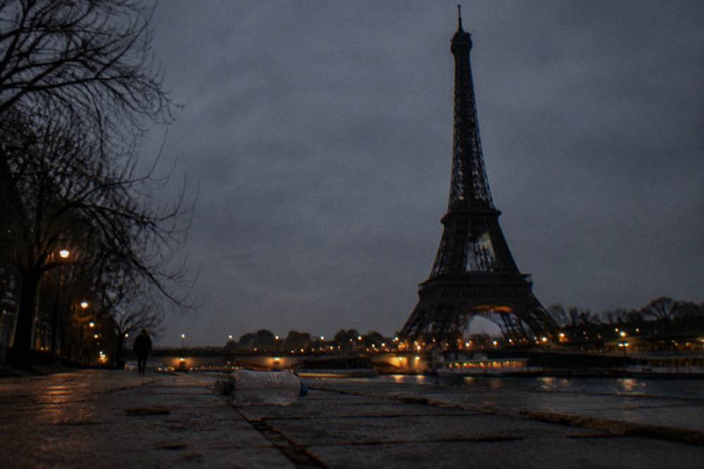 The Eiffel Tower as a dark silhouette against the night sky above empty Paris quays
