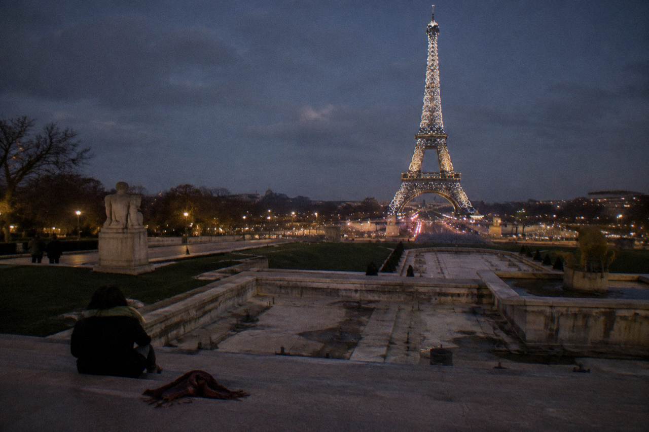 The Eiffel Tower glowing gold against a dark evening sky above Paris rooftops