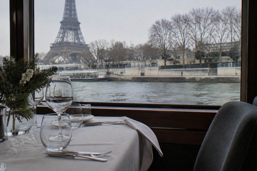 A set dinner table with glassware beside a window reflecting evening city lights