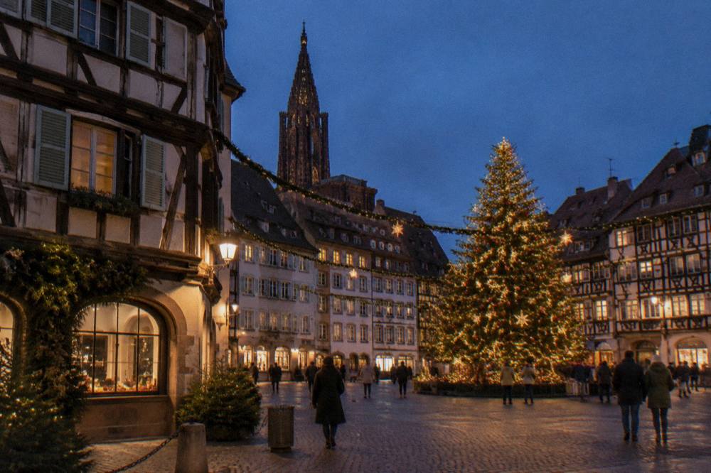 Timber-framed Alsatian buildings decorated with garlands and a Christmas tree at night