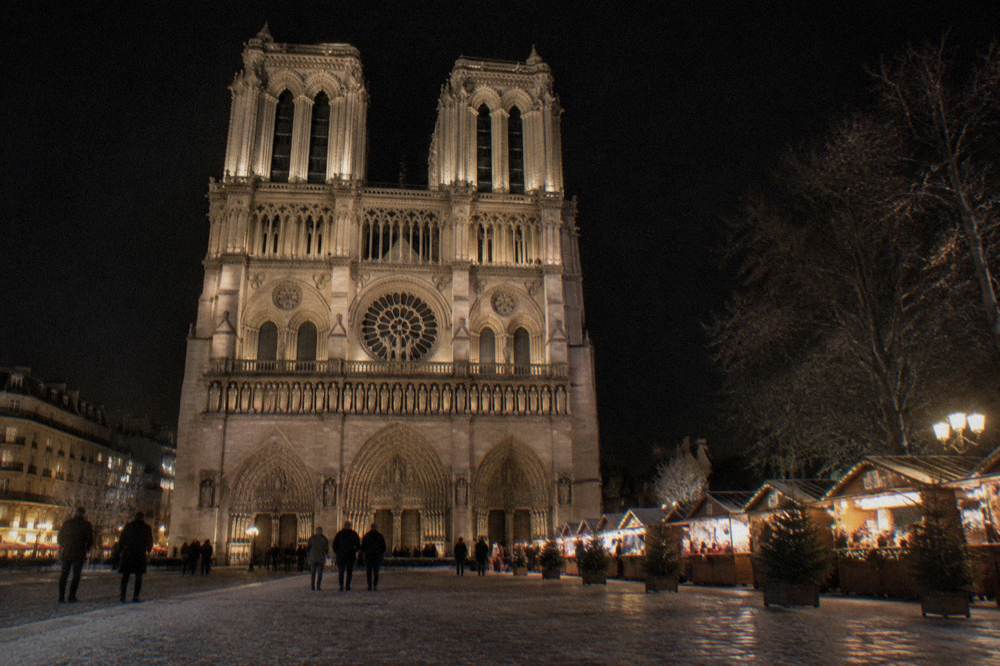 Floodlit Gothic cathedral facade above a Christmas market at night