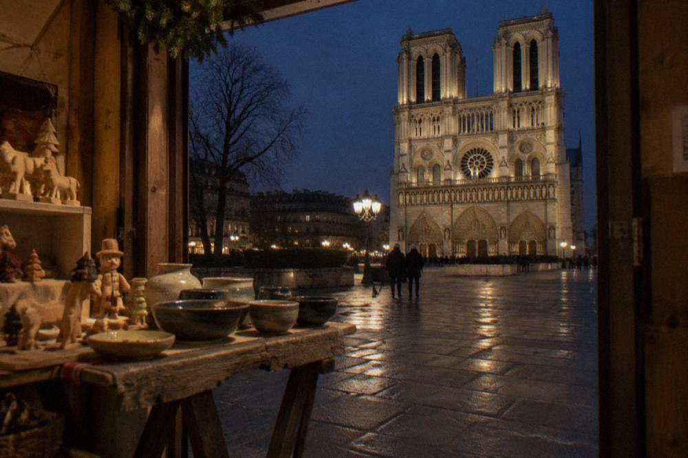 Small market chalets with handcrafted goods facing a floodlit cathedral facade at night