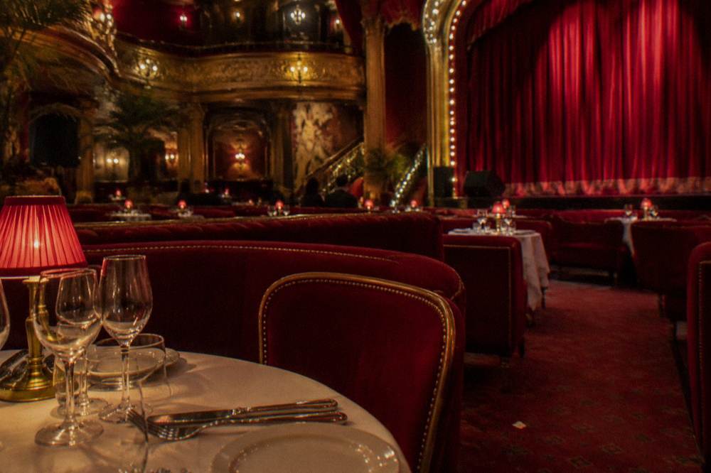 A cabaret dining room with red velvet seating and tables set for dinner before a show