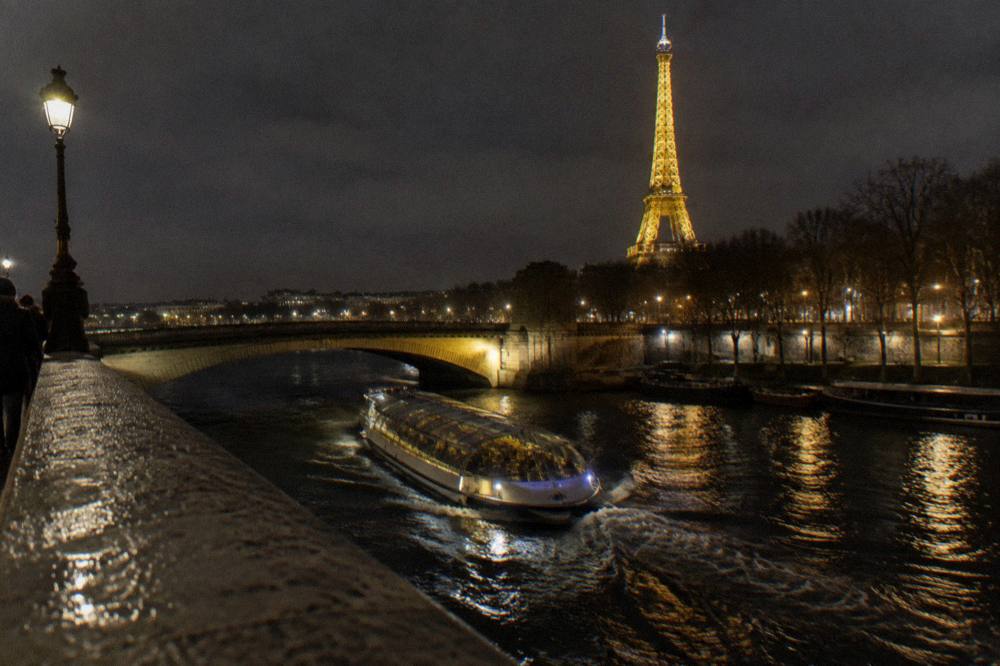 A covered boat passing illuminated bridges on the Seine at night