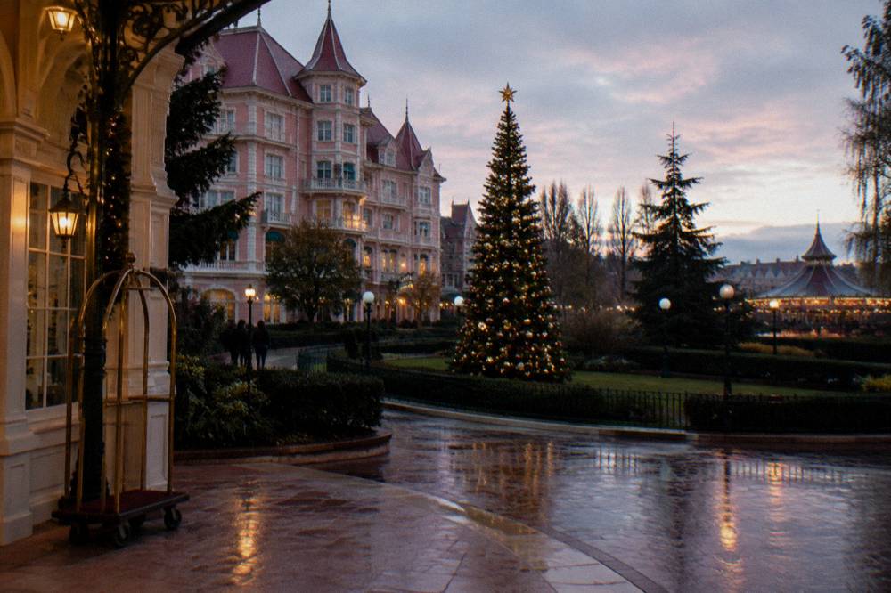 A festive theme park entrance at night with illuminated decorations and crowds of visitors departing