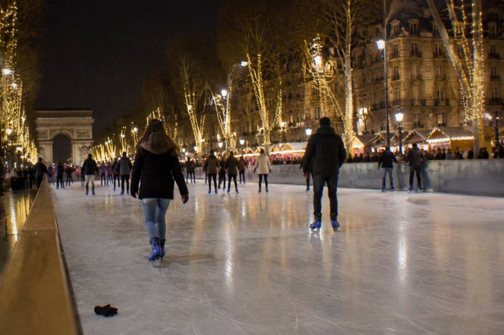 Skaters gliding across a floodlit outdoor rink between tall illuminated trees