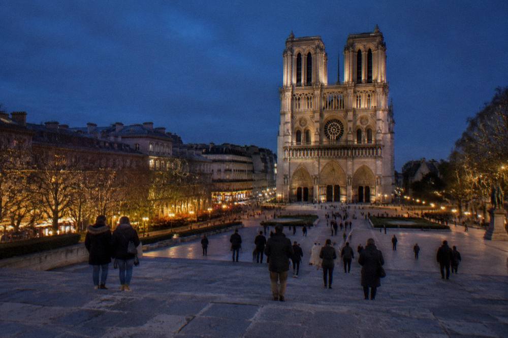 The floodlit Gothic facade of Notre-Dame cathedral seen from the parvis on a December evening