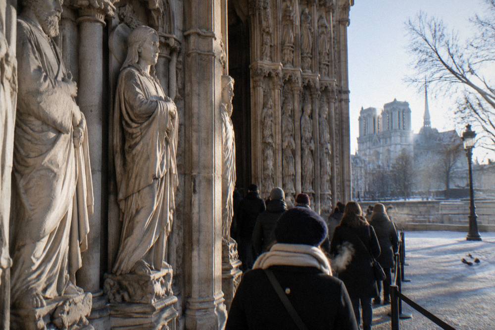 The entrance portal of Notre-Dame cathedral with visitors waiting in a reservation queue