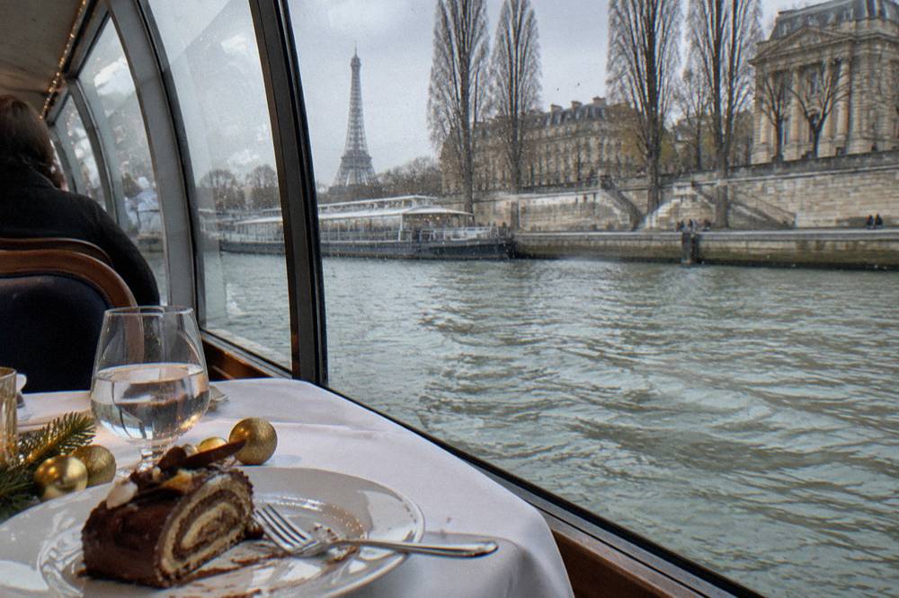 A set lunch table with festive decorations beside a window overlooking the Seine