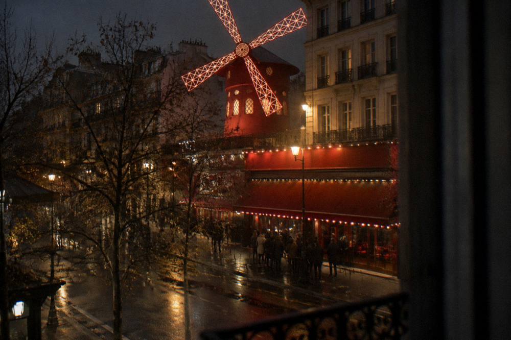 A red windmill facade lit at night on a Paris boulevard with a small queue outside