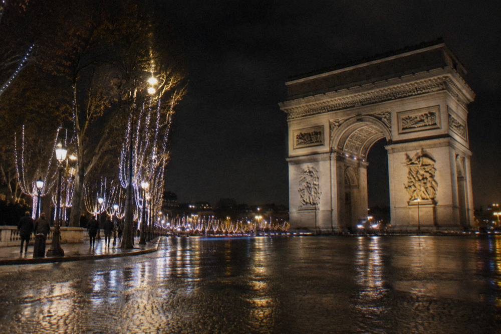 Garland-lit trees lining the Champs-Élysées at night with the Arc de Triomphe glowing at the far end