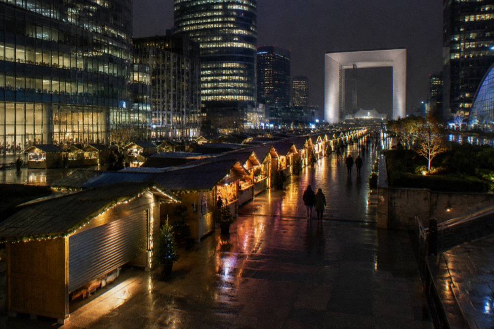A wide modern esplanade lined with illuminated market chalets at night