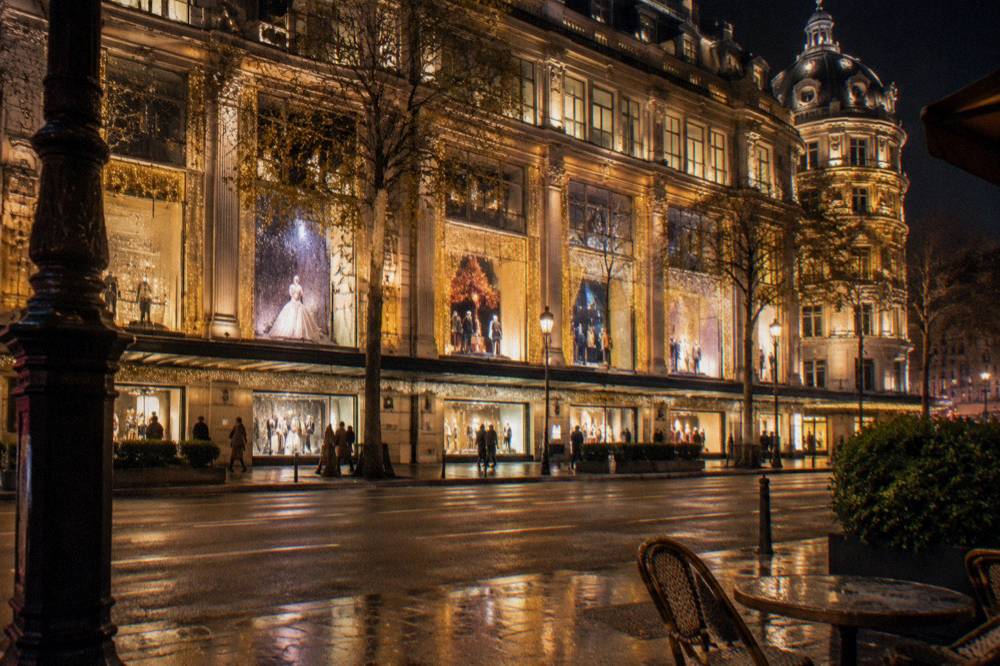 Department store facade decorated with festive lights and window displays on a Paris street at night