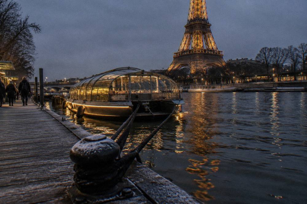A boat with bright lights moored on the Seine at night with ornate bridges in the background