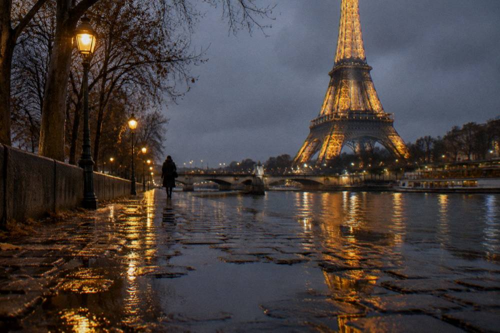 A riverside quay at night with wet cobblestones reflecting golden lamplight