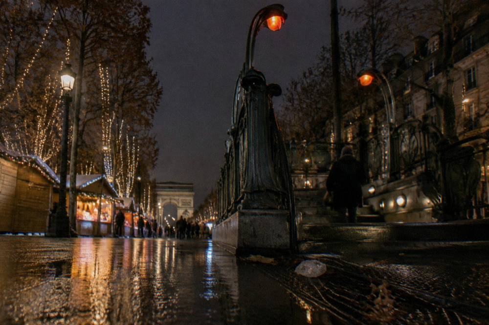 Illuminated Paris metro station entrance at night with a decorative street lamp above