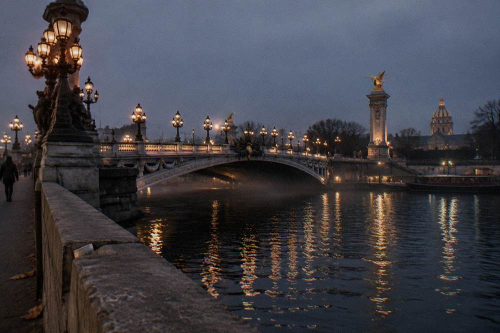 Lit bridge over the Seine at night seen from the riverbank
