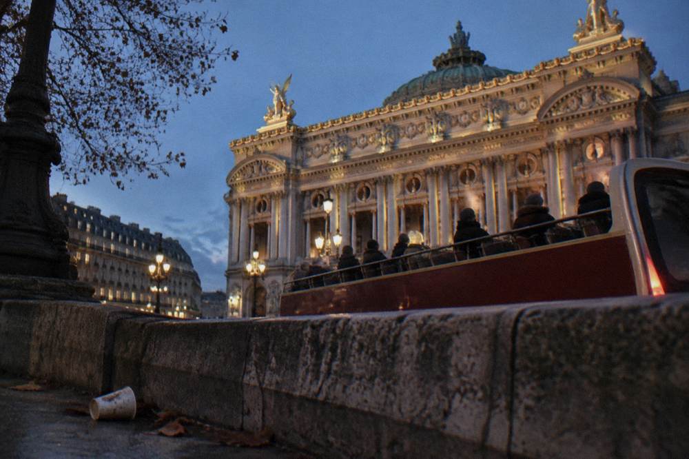 Open-top tour bus passing illuminated buildings on a cold clear evening