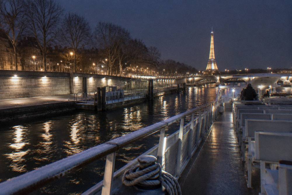 An open-top river boat moored at a lit stone pier on the Seine at night in winter