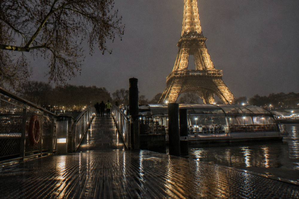 A lit boarding gangway and pontoon on the Seine at night with a covered boat waiting at the pier