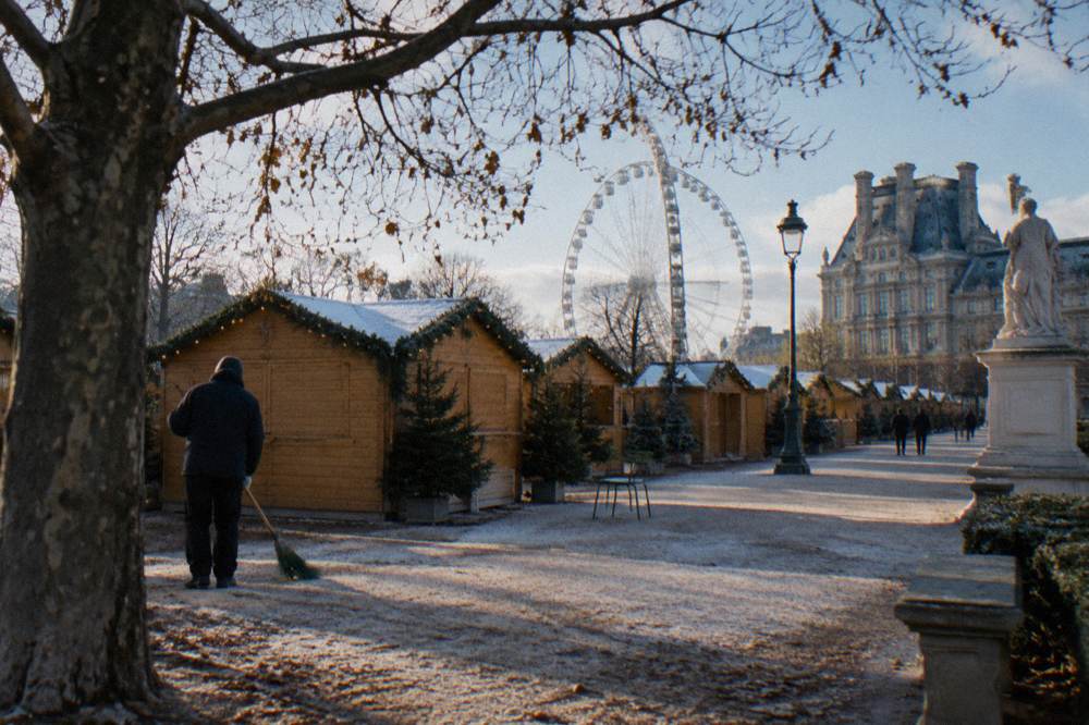 Wooden market chalets with glowing garlands and a ferris wheel behind them in a Paris garden